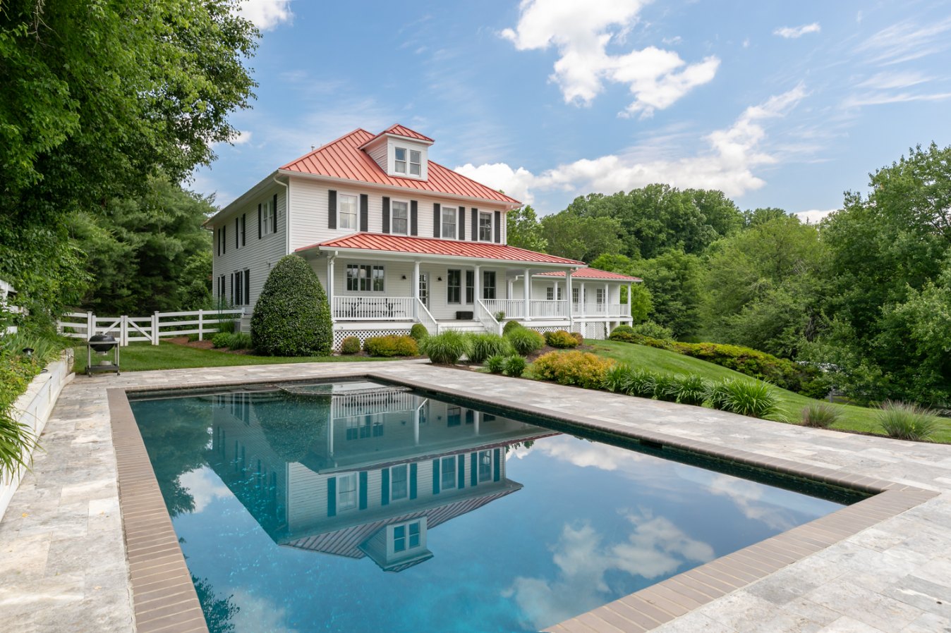 White colonial home with a red metal roof and a swimming pool